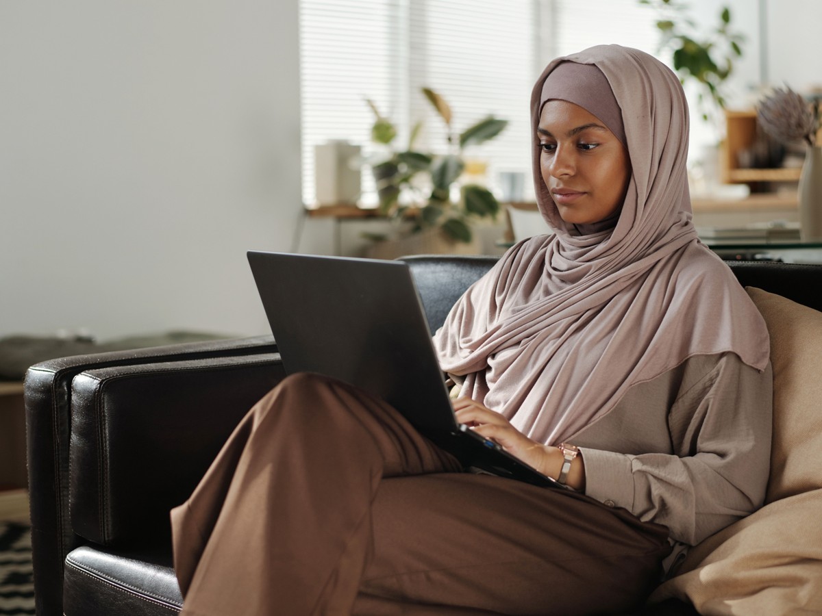 A young woman wearing a headscarf working on a laptop