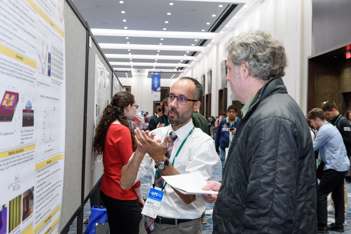 A Black physicist presenting a poster to a scientific meeting attendee
