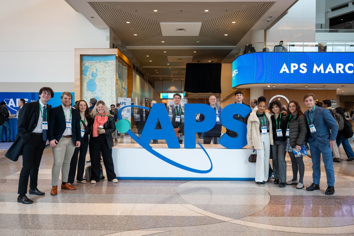 APS March Meeting attendees pose in front of an APS logo display.