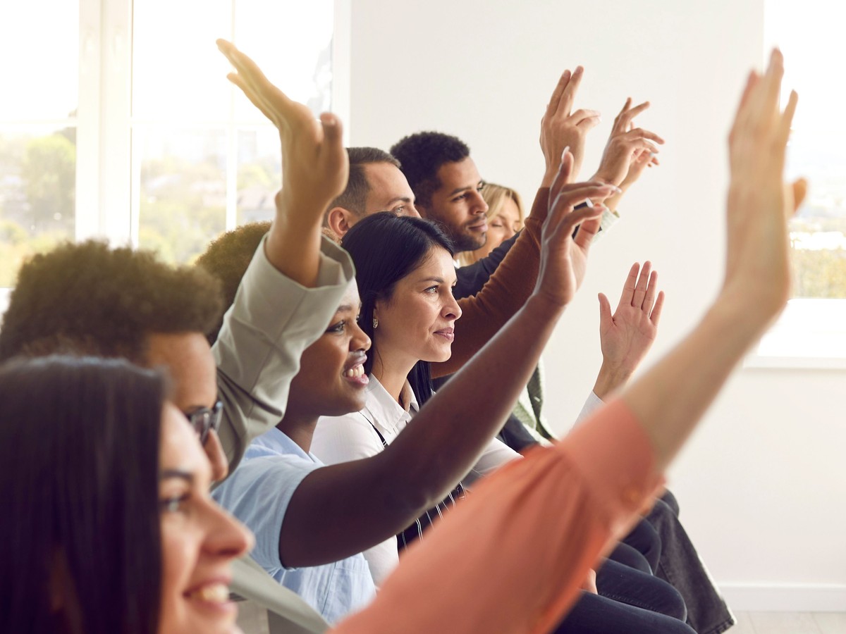 A group of racially diverse students raising their hands in a sunny classroom
