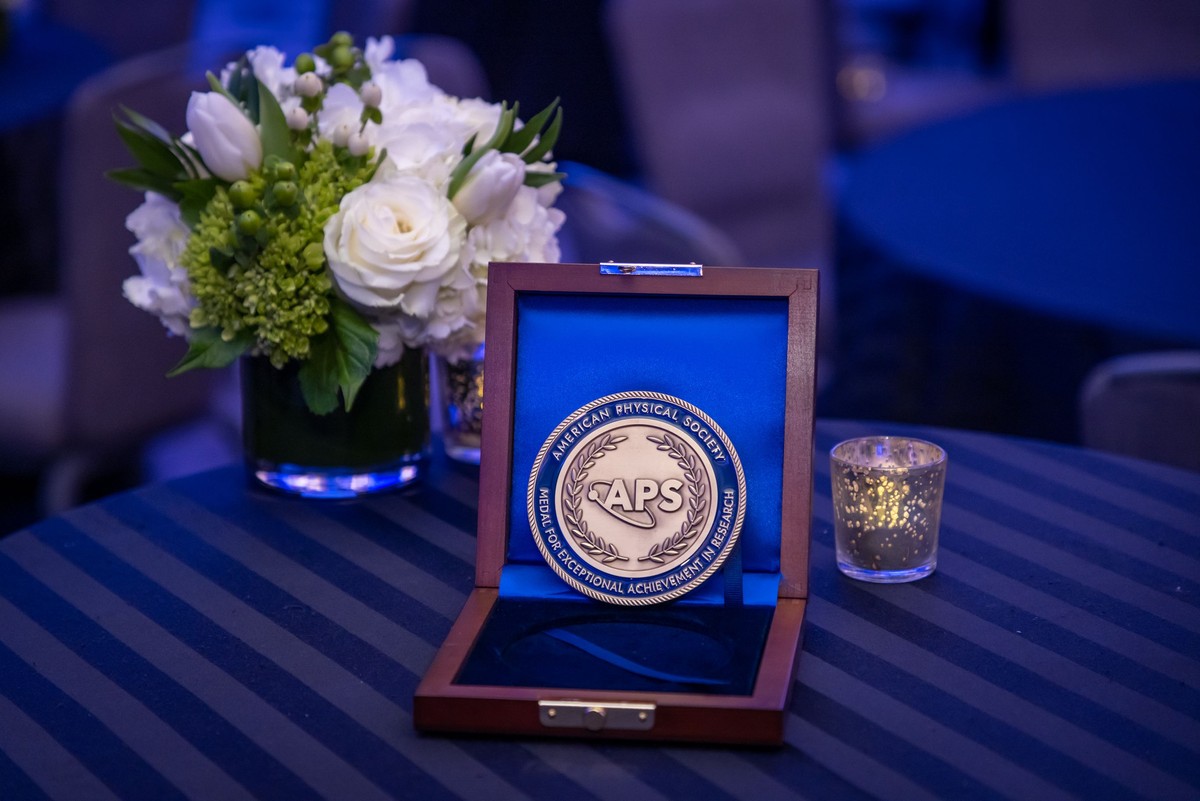 APS medal in an open wooden box on a table with a boquet of white flowers and a candle in the background