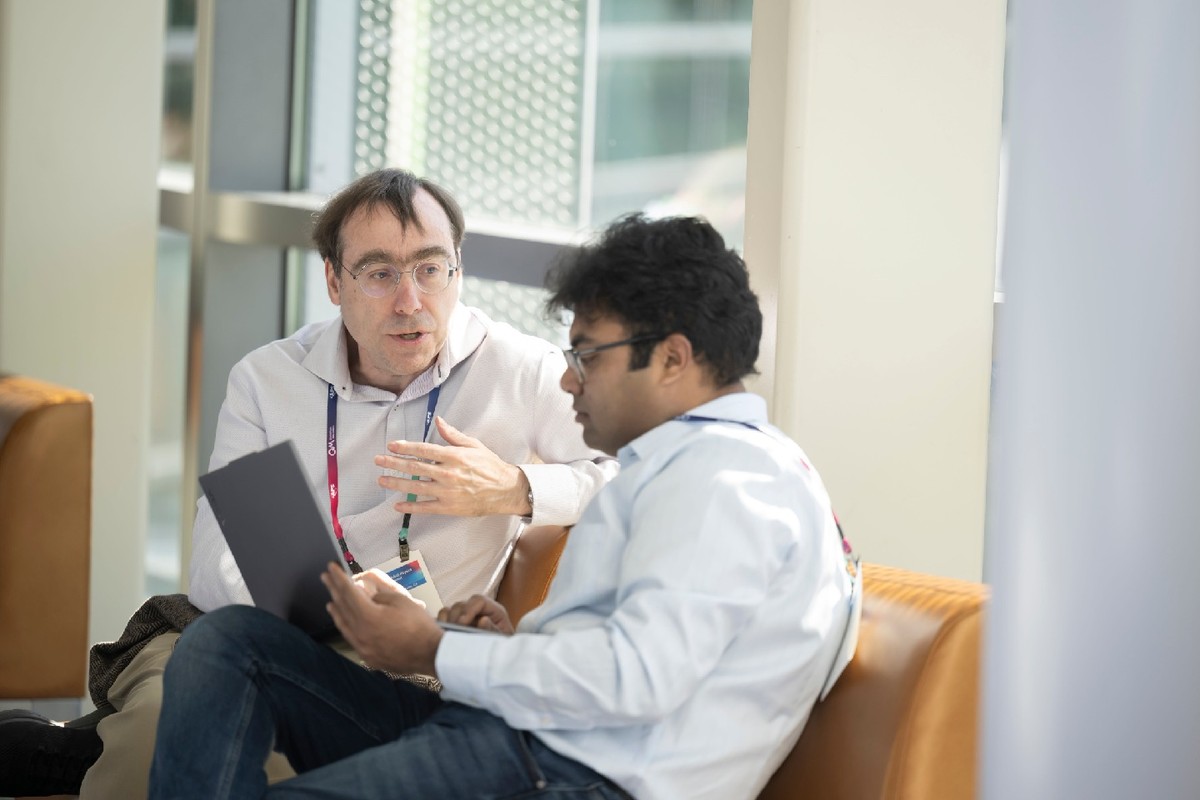 Two men sitting next to each other white button-down shirts in conversation.