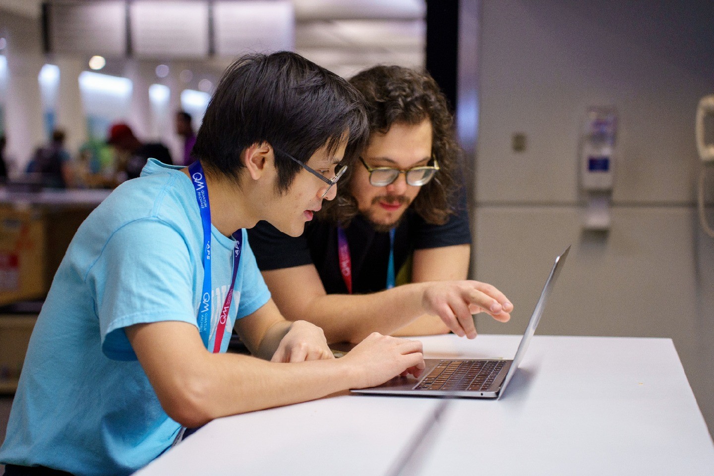 Two young men wearing conference lanyards look at a laptop together.