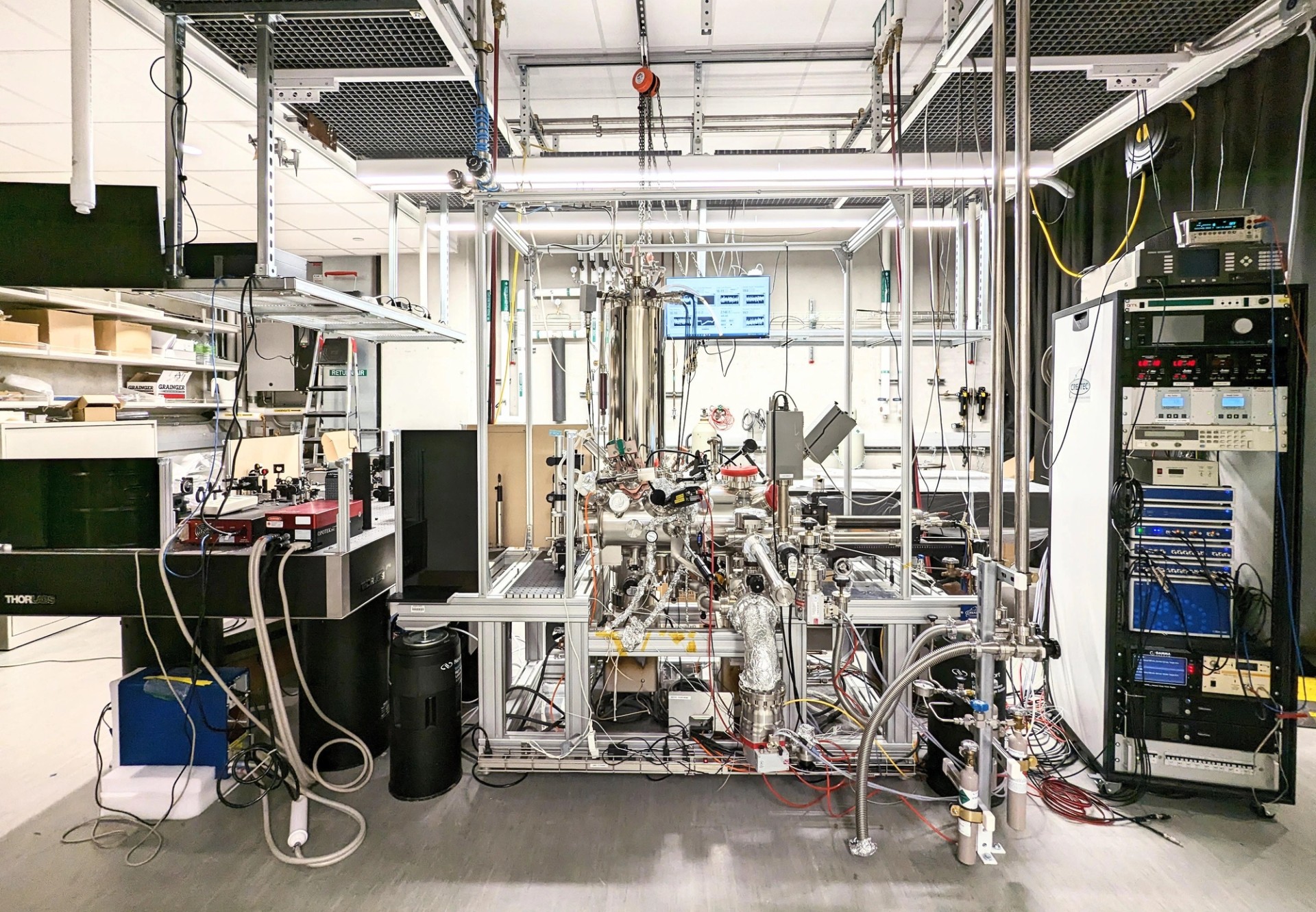 Silver, shiny laboratory equipment, with many tubes and wires, appears to fill part of a room.