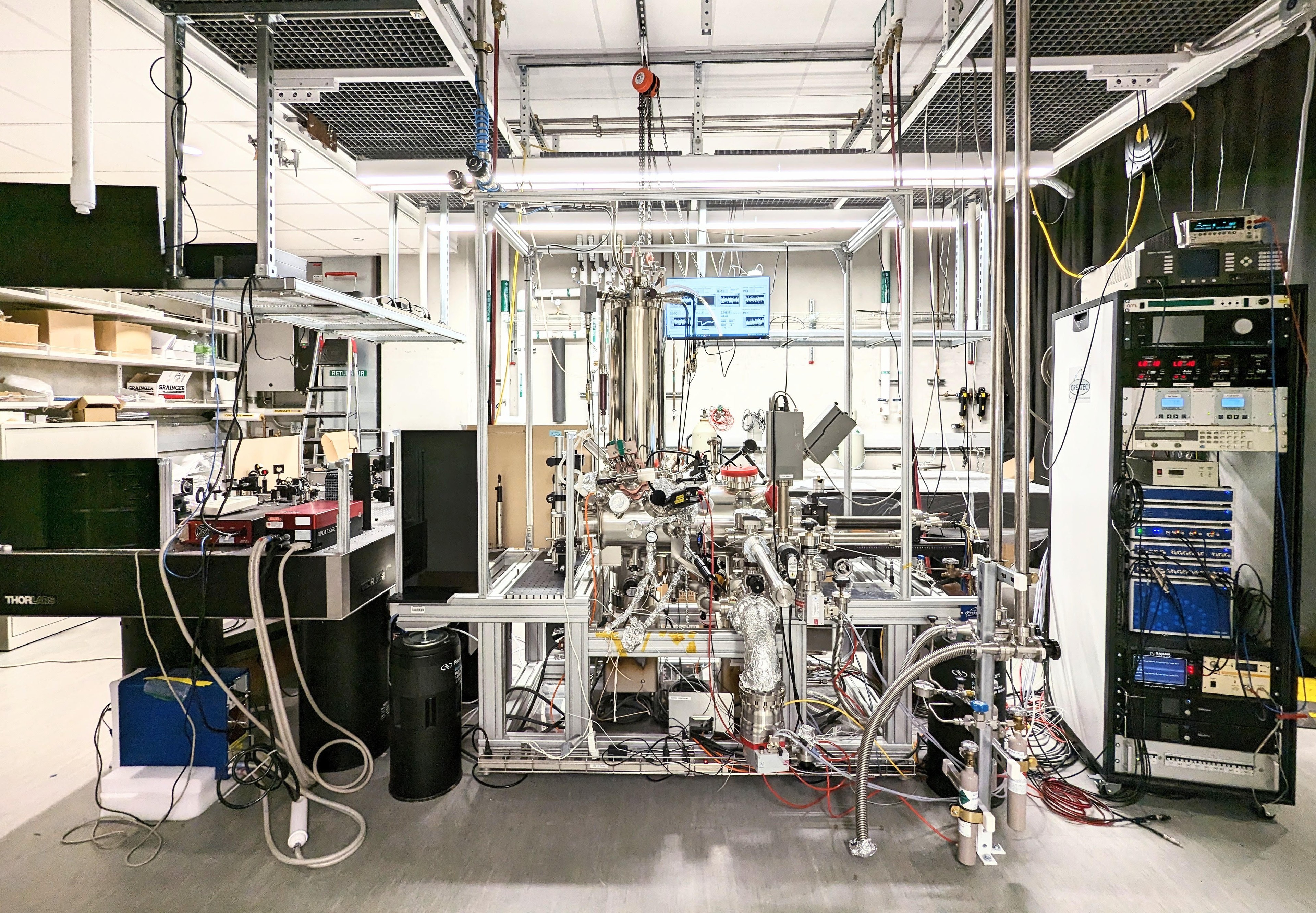 Silver, shiny laboratory equipment, with many tubes and wires, appears to fill part of a room.
