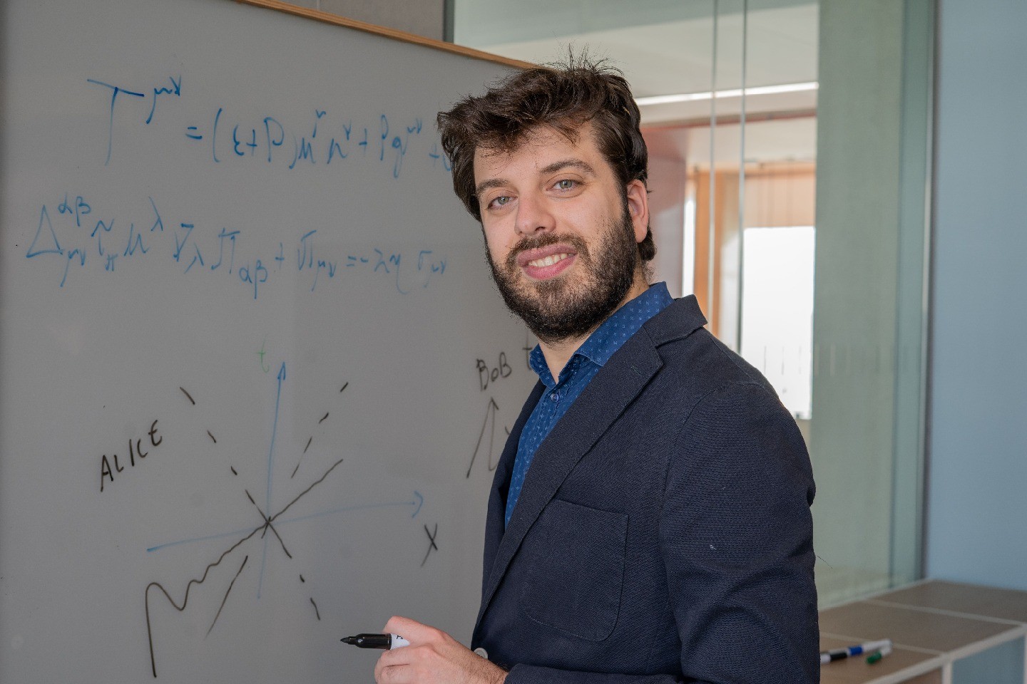 Lorenzo Gavassino stands in front of a whiteboard with equations, a marker in his hand.
