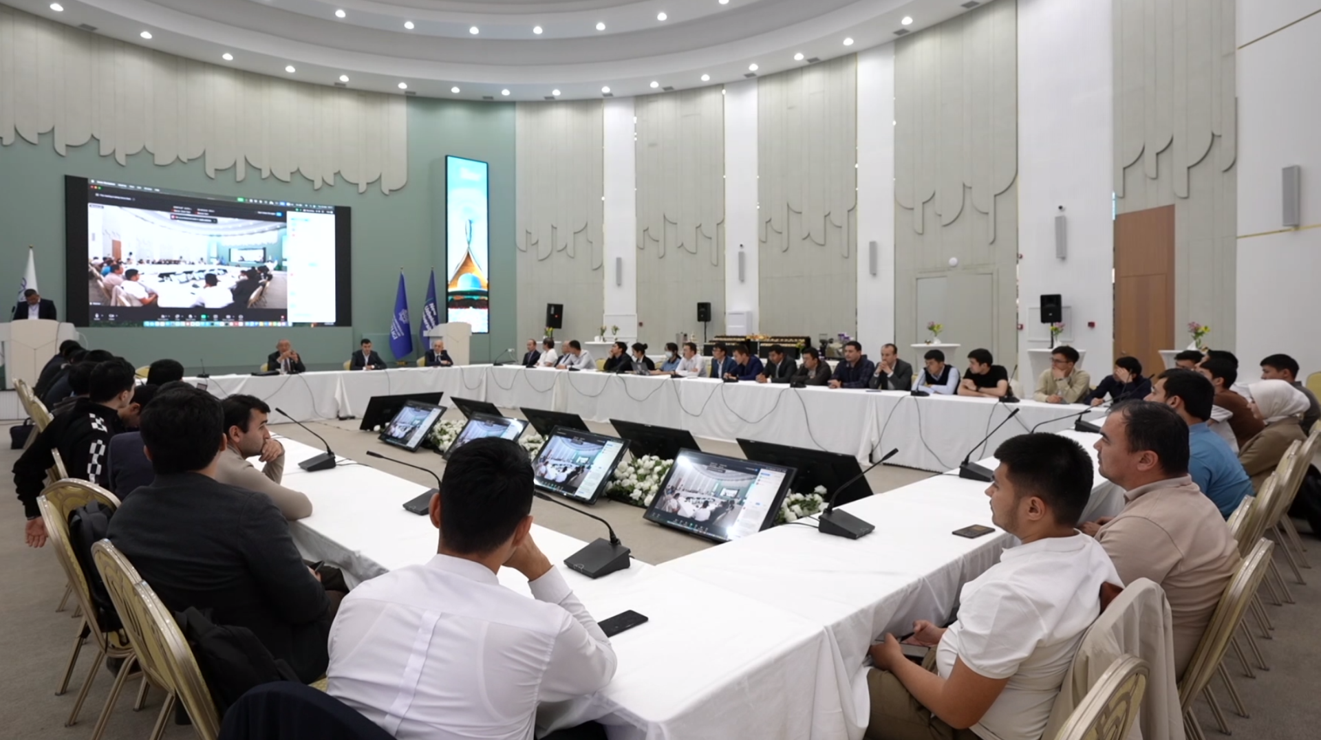 Meeting attendees sit at four tables arranged in a square, round table style and facing one another.