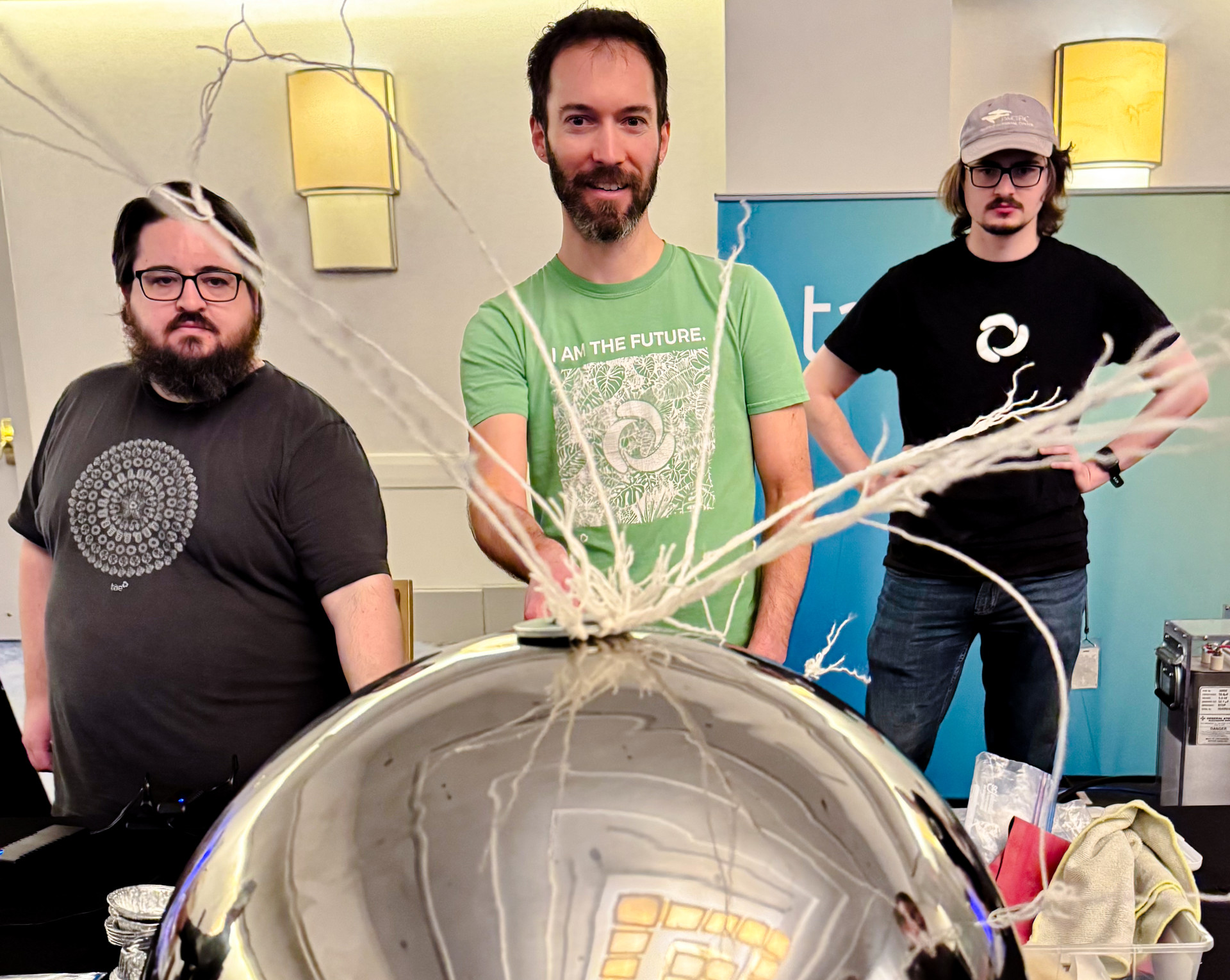 Three volunteers stand behind a Van de Graaff generator as it creates static electricity.