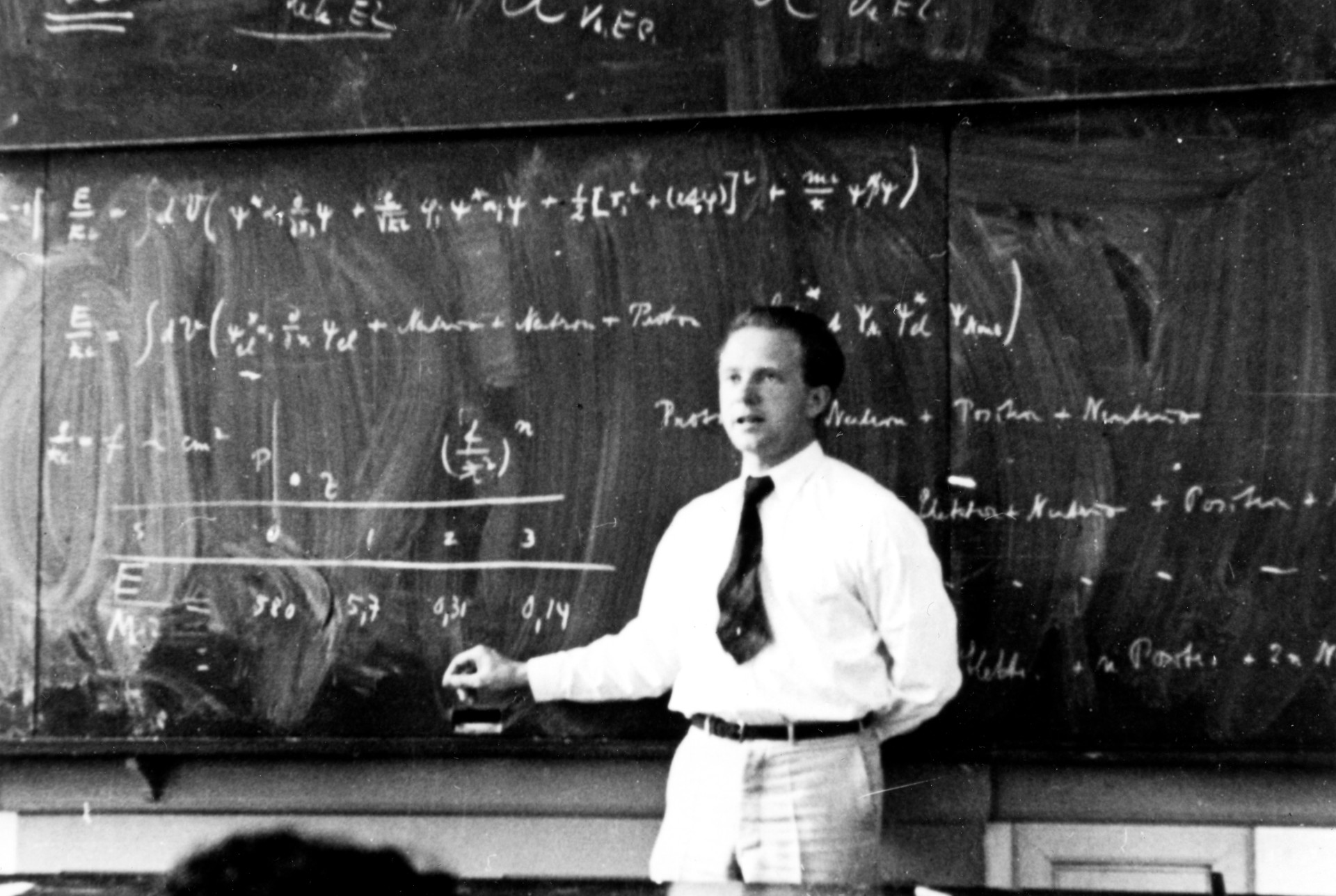 A photo of Heisenberg standing in front of a blackboard covered with equations.