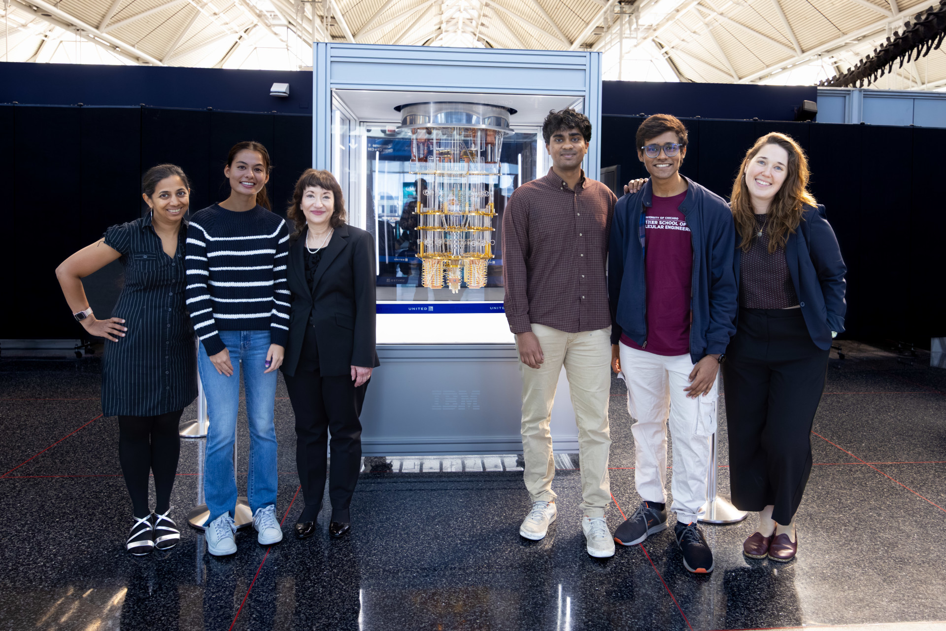 The six project colleagues pose in front of the newly unveiled quantum computer, housed in a large case.