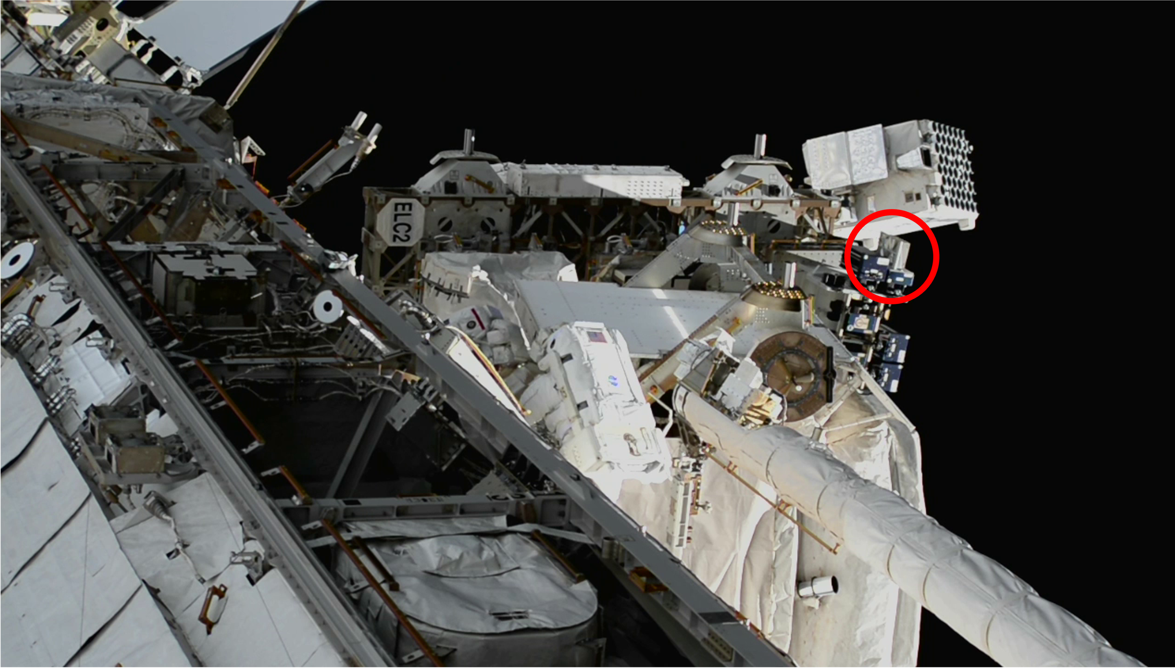 Close-up view of the International Space Station exterior, showing equipment and, circled in red, SEAQUE. An astronaut in a spacesuit in the middle of the photo blends into the white station structures.