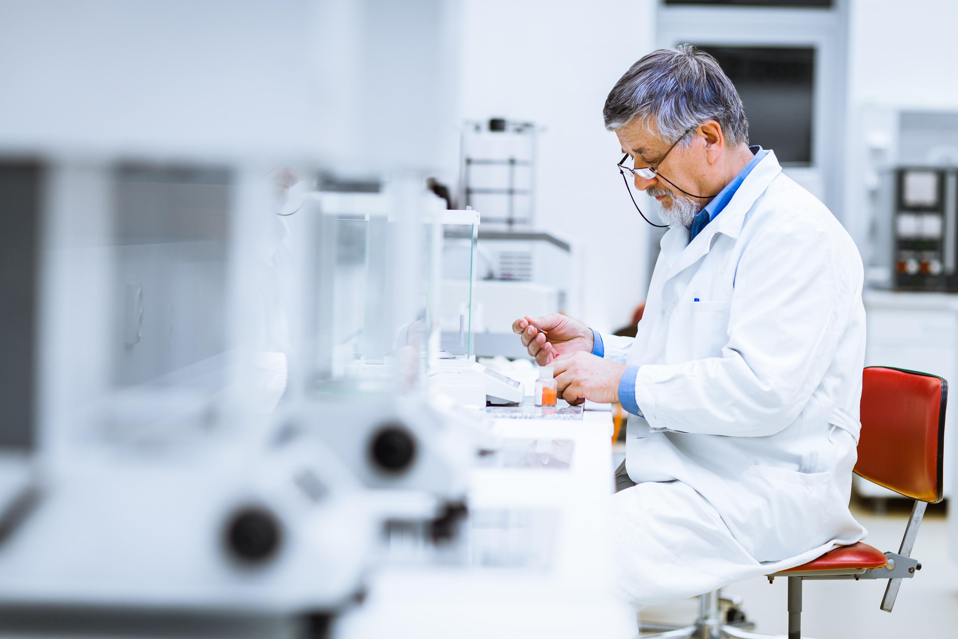 A scientist sits at a lab bench in a white coat, working.