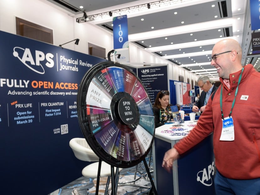 APS meeting attendee at a Spin to Win wheel in front of an Open Access backdrop.